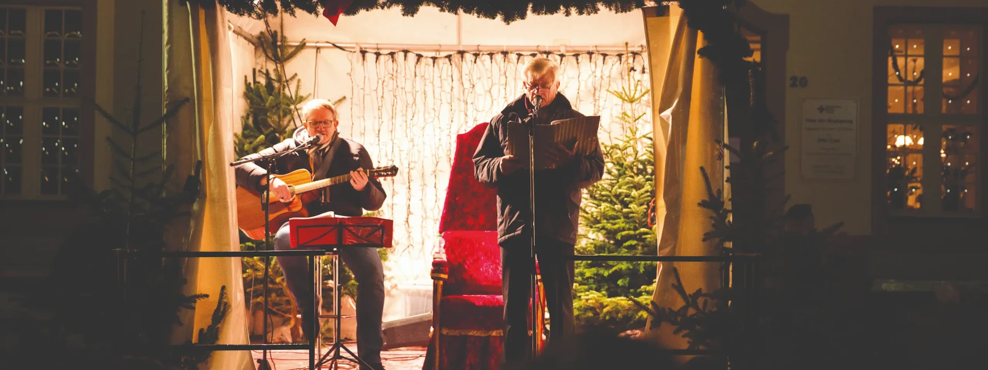 Liederabend mit Gniffke © Henry Tornow Zwei Männer auf einer Bühne in weihnachtlichem Ambiente und mit einer Gitarre und einem Liederheft © Henry Tornow