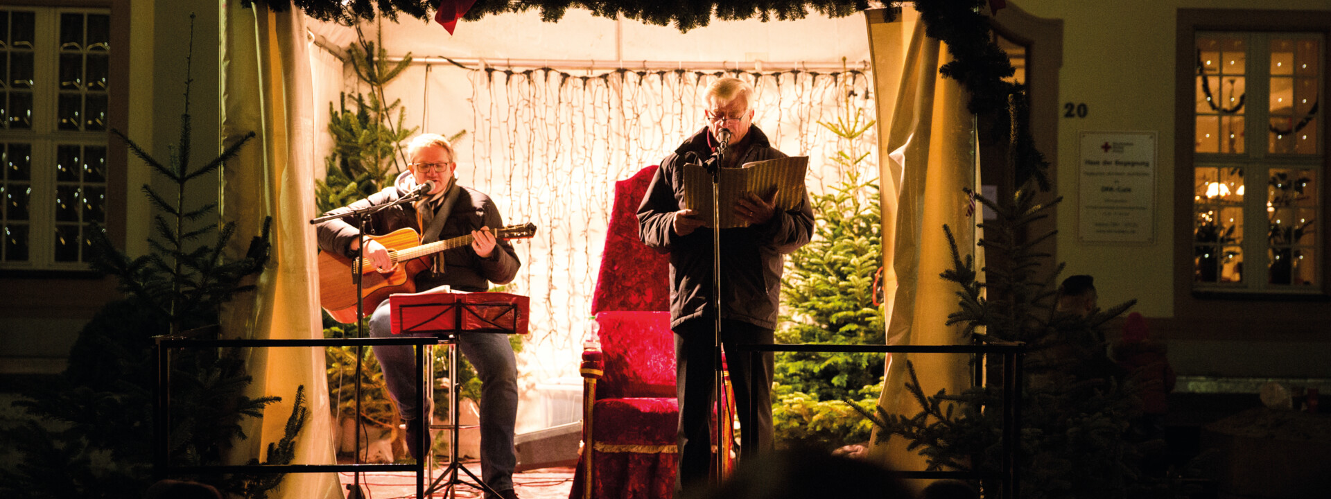 Zwei Männer auf einer Bühne in weihnachtlichem Ambiente und mit einer Gitarre und einem Liederheft © Henry Tornow